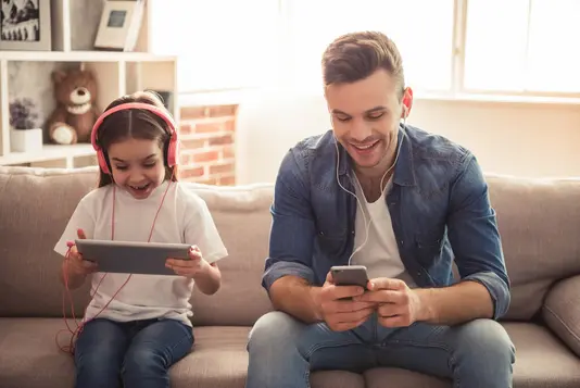 Haus-Familie-Wohnen-Serie-12-27 Vater und Tochter sitzen auf der Couch und hören Musik mit Kopfhörern.